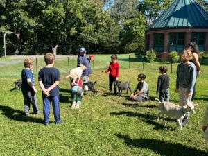 children, goats, and goatkeepers on a grassy lawn