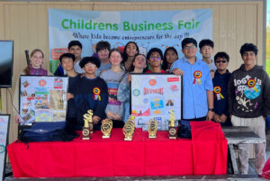 A group of volunteers stands behind a table that holds a variety of award trophies.