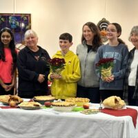 A group of people behind a table, on which there are a variety of apple pies