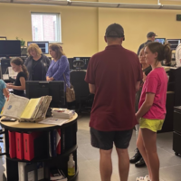 Adults and children mingle informaly with uniformed police officers in a room with multiple computer displays