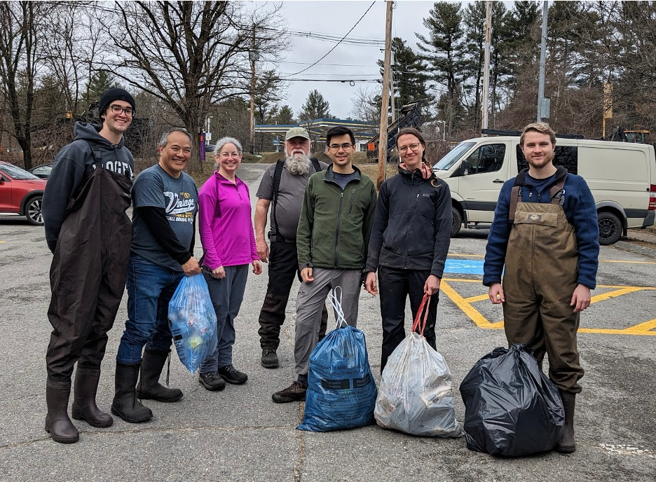 A group of people in a parking lot with bags of trash that was cleaned from a wildlife area