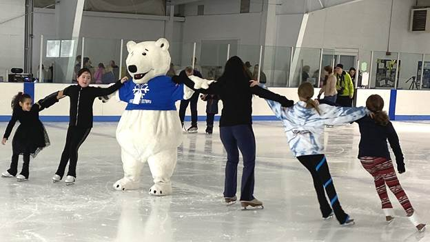 Ice skaters hold hands with a mascot bear