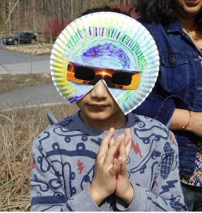 person wearing eclipse glasses with a paper plate art surround.