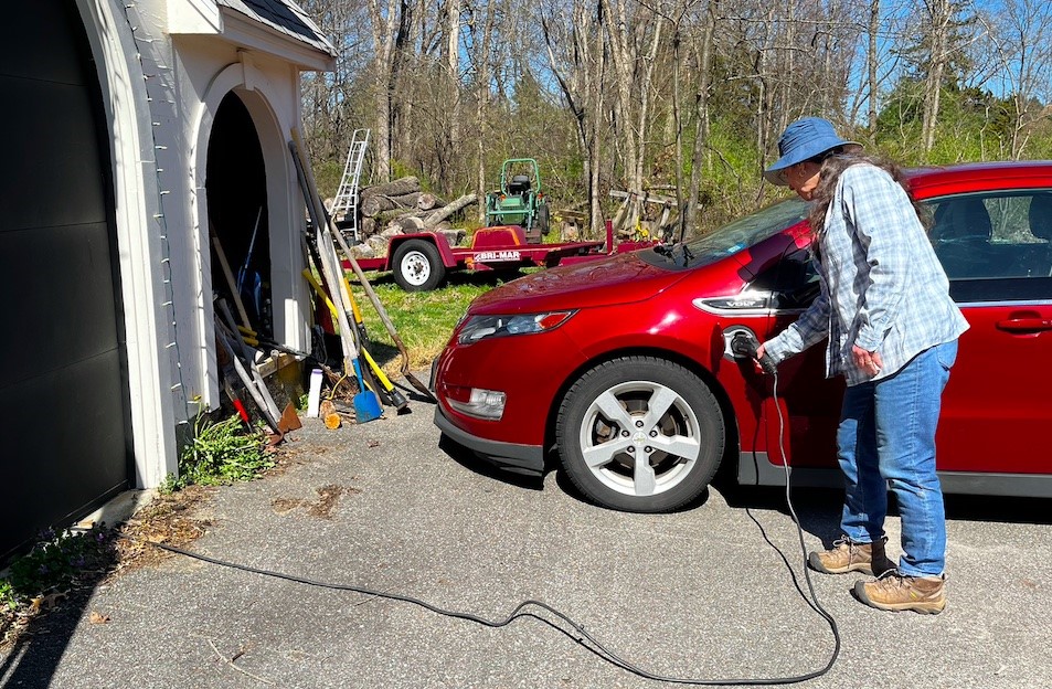 Woman inserting a charger into a Chevy Volt. The power cord snakes into the garage.