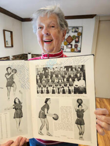 Woman with gray hair proudly shows off the basketball page from her high school yearbook (circa 1955).