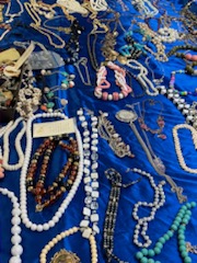 A large number of necklaces and bracelets spread out on a blue tablecloth