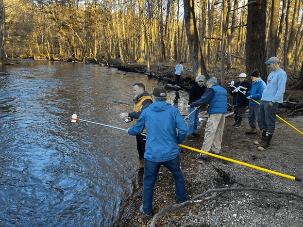 A group of people on the shore holding long poles with bottles at the end.