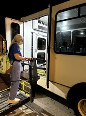 Woman in a blue t-shirt uses the lift to board the bus home from Town Meeting.