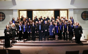 A group of adults stand on a church dias, looking like they are ready to burst into song.