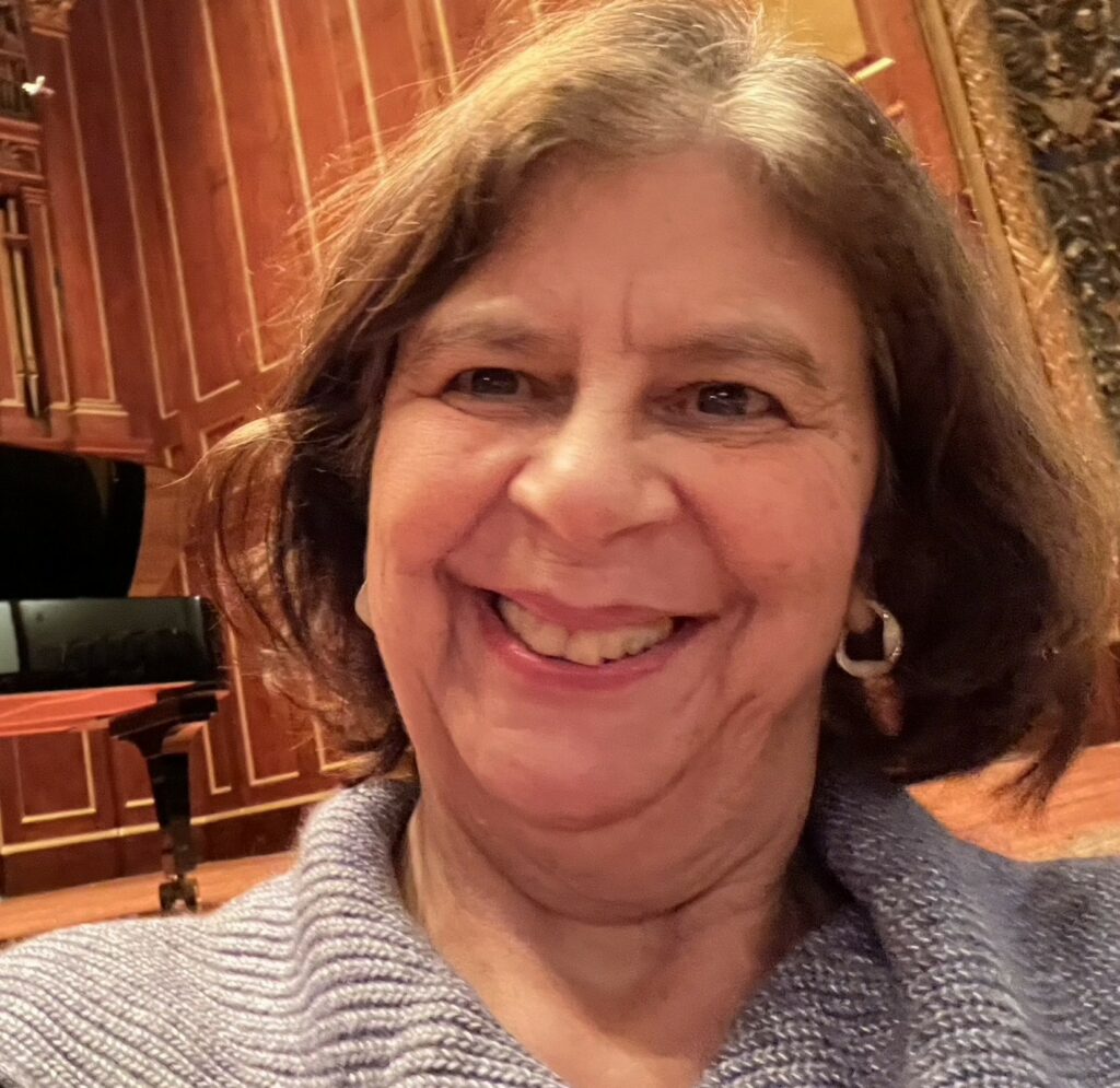 Smiling woman with medium length brown hair. A piano is in the background.