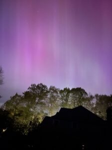 A multi-colored sky shows behind houses and trees.