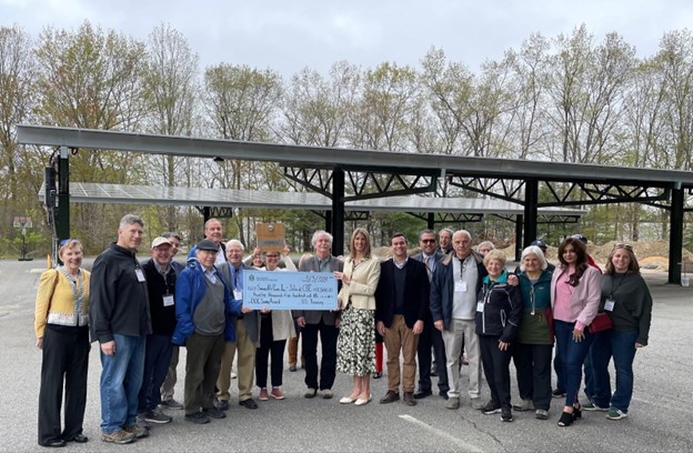 With two of the three community solar carports in the background, U.S. Representative Lori Trahan presents the Dept. of Energy SUNNY Award for Equitable Community Solar to members of Congregation Beth Elohim and their supporters