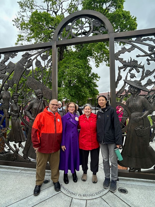 Four people stand in front of Meredith Bergmann's sculpure. The sculpure is a bronze gate, with images of women in Lexington's history depicted in the design.