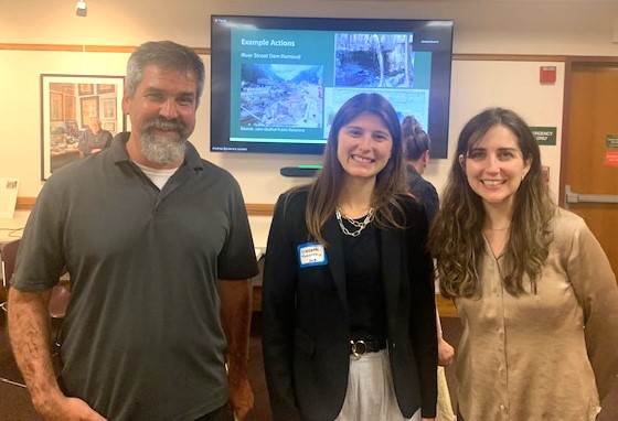 A bearded man and two women with long brown hair pose in front of a screen that says "Example Actions" and contains images.
