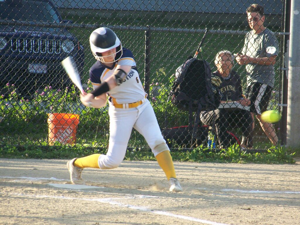 A young woman in a Revs uniform swings a bat.