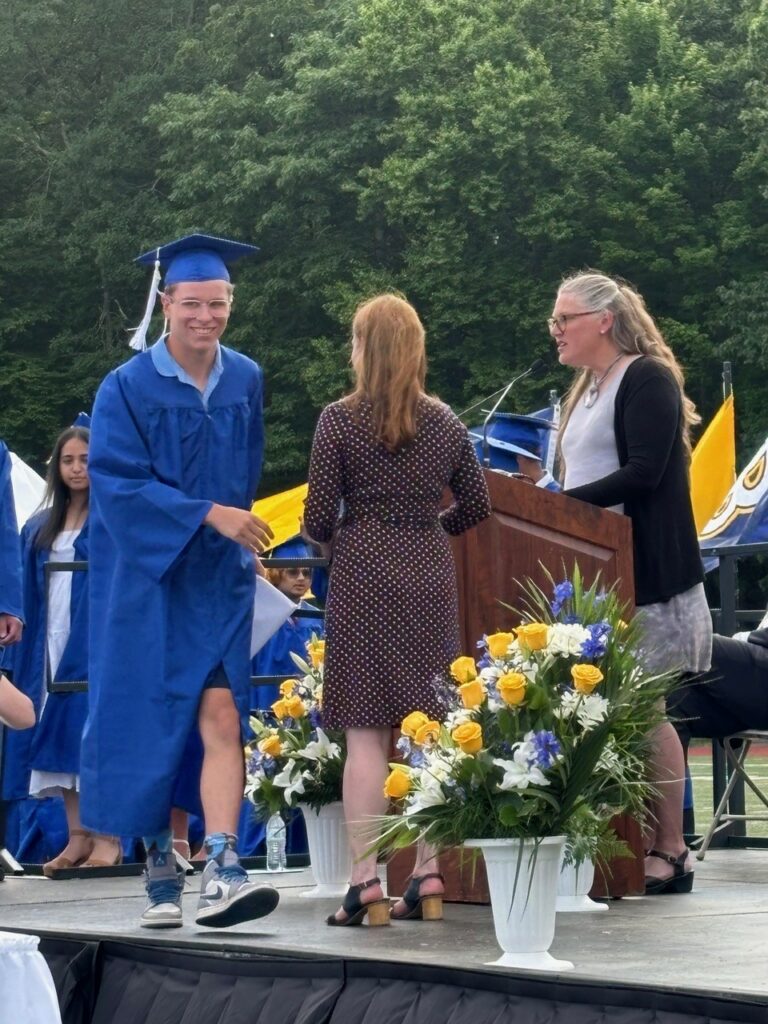 A smiling young man walks across the stage to get his diploma.