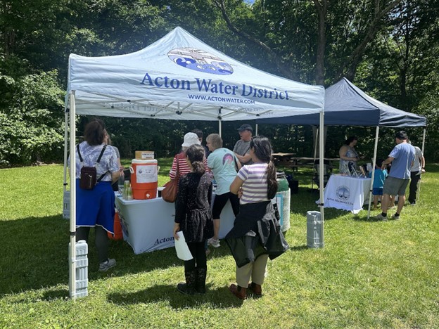 Another booth -- the awning says Acton Water District. There are people behind the table talking to a group of fair attendees.