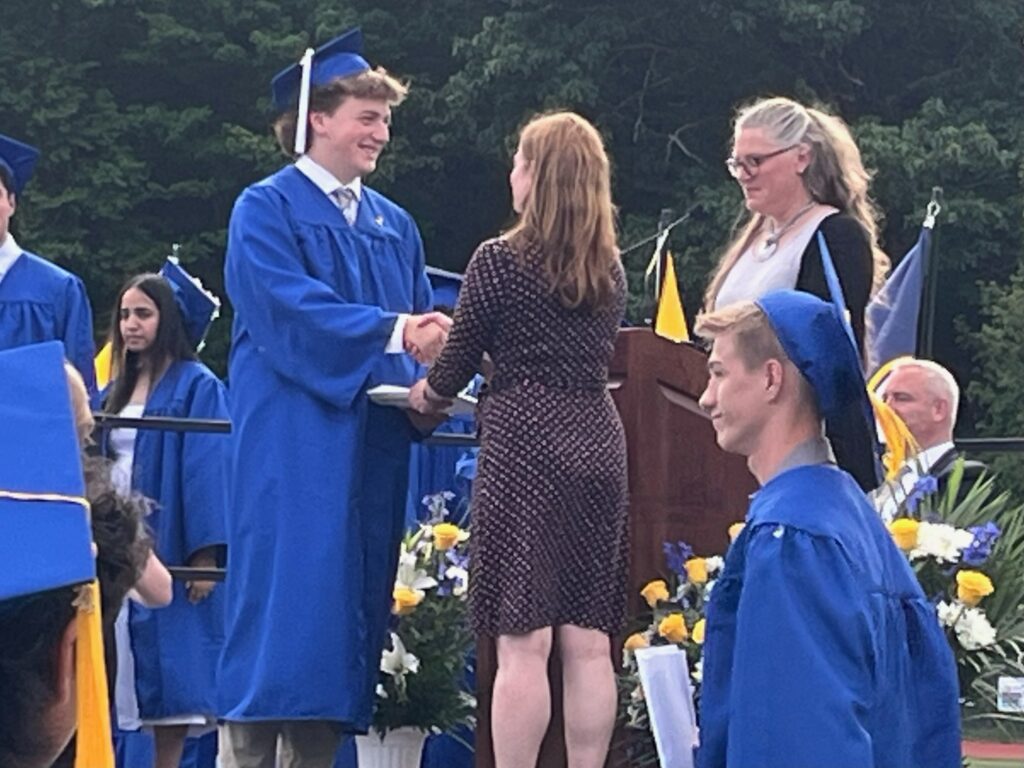 A young man in a blue cap and gown shakes hands with the Acton Boxborough principal.