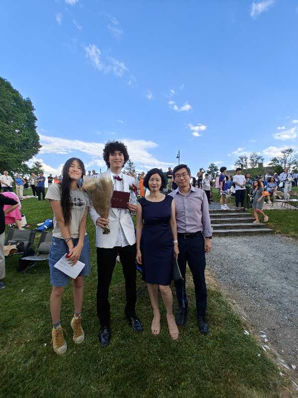 A family of four poses. The graduate is holding roses and his diploma. Like other Weston High School graduates, he is wearing a white formal jacket with a red bow tie.