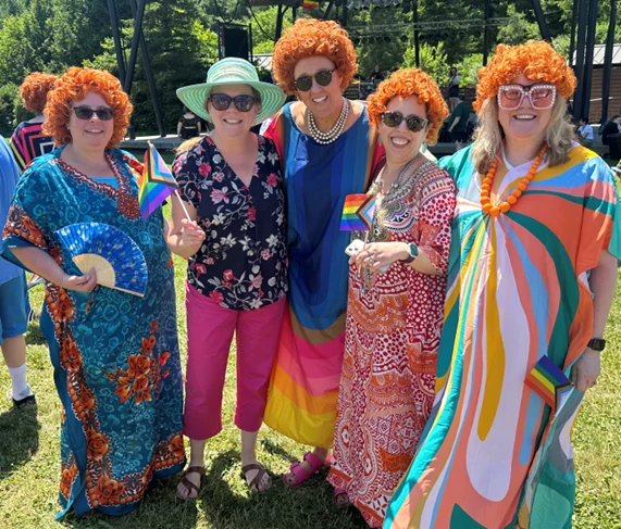 Five women posing in the sun. Four of the women are wearing Helen Roper costumes -- Curly red wigs, bright kaftans, and chunky jewelry. The 5th woman is wearing a straw hat and sunglasses, as befits the perfect weather.