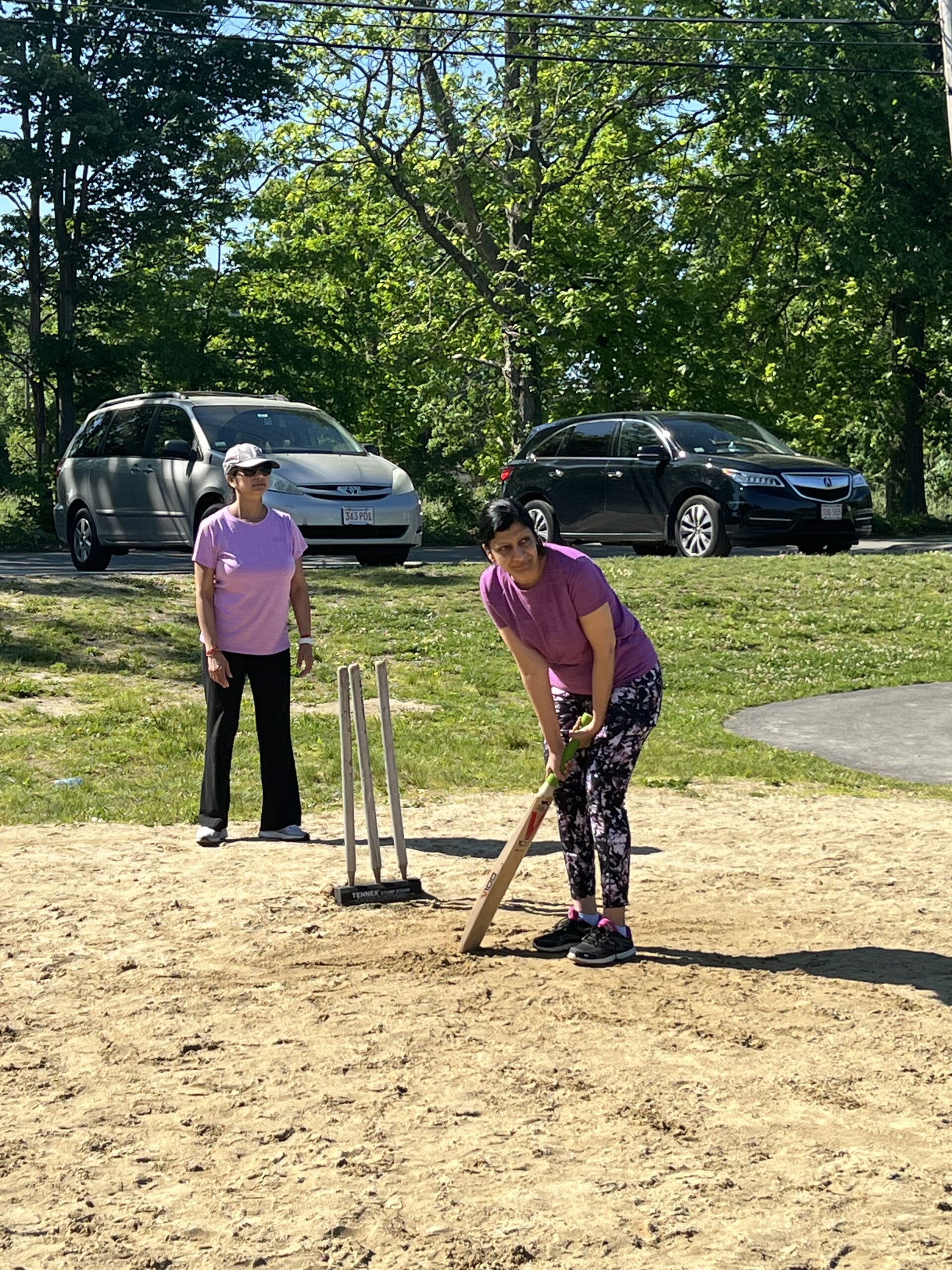 Two women on a cricket pitch. One is batting, and one is standing behind the wicket (similar to a baseball batter and catcher, but different).