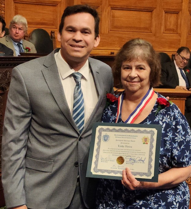 A smiling man and woman stand together. The woman is proudly holding a certificate.