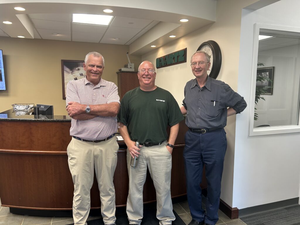 Three older men smile at the camera.