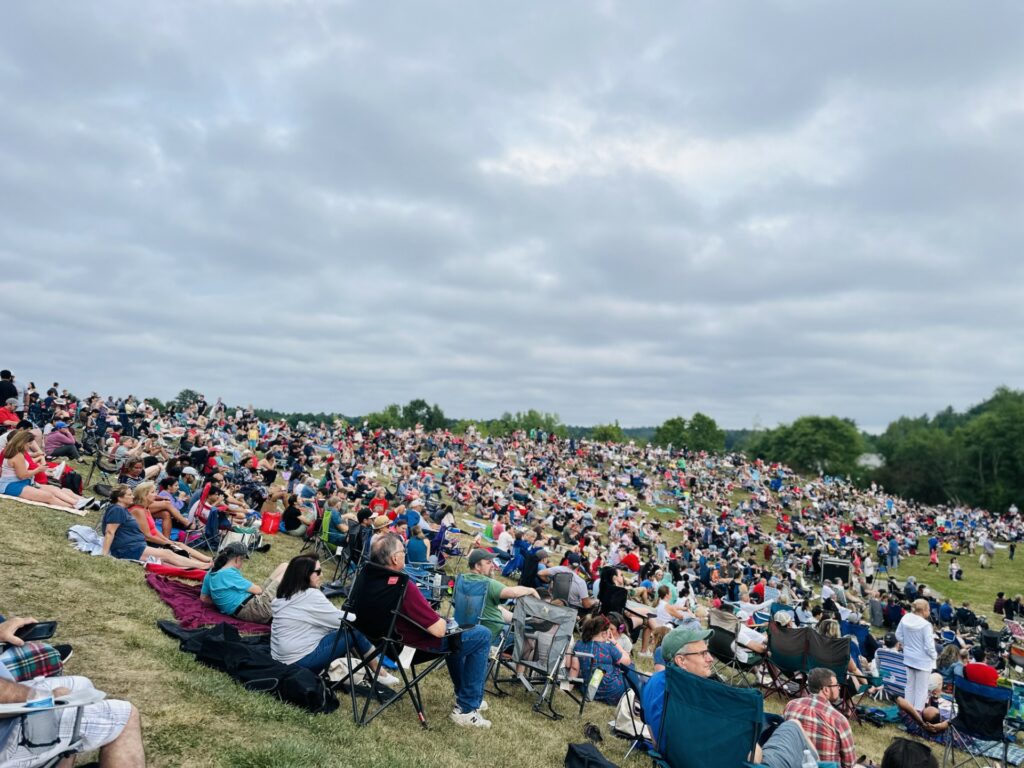 Crowds of people sit on a hill under a slighly cloudy sky.