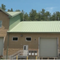 A light tan industrial-type building with a green roof. There are several small windows and two large bay doors.