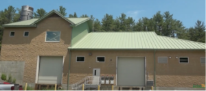 A light tan industrial-type building with a green roof. There are several small windows and two large bay doors.