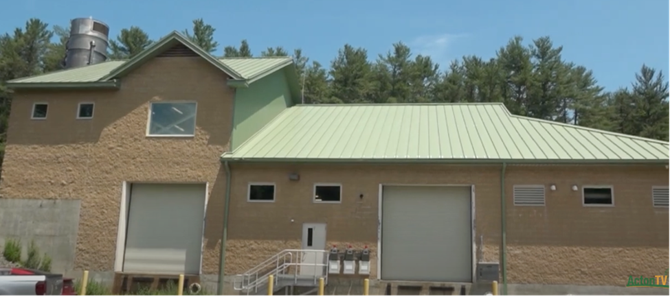 A light tan industrial-type building with a green roof. There are several small windows and two large bay doors.