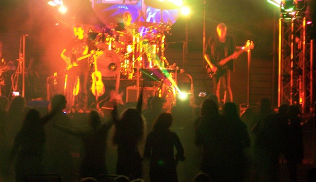 The band is lit up with red lights and dancers show in silouette in the foreground.