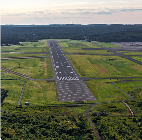 An airport runway surrounded by green fields and forests in the background.