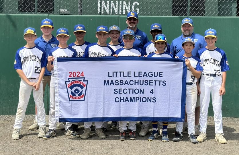 A group of boys (and two men) wearing Acton-Boxborough baseball uniforms and hats proudly holds a banner that proclaims " Little League Massachusetts Section 4 Champions."