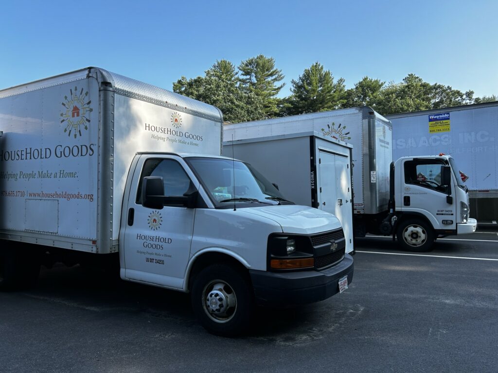 Several trucks are lined up in the Household Goods parking lot. On the front truck, you can see the Household Goods logo and label.