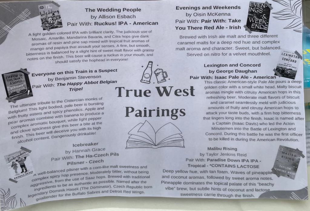 A small poster stands by stacks of books. Some of the suggestions include pairing "The Wedding People" by Allison Esbach with True West's Ruckus! IPA or "Lexington and Concord" by George Daughan with Isaac Pale Ale.