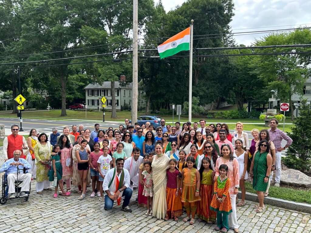 A large group of people pose in front of the Indian Flag.