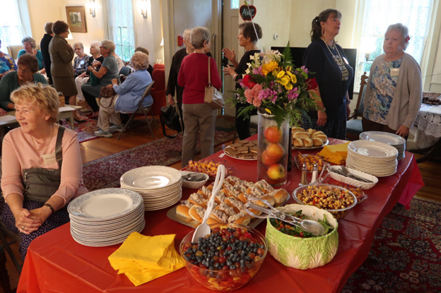 A lovely buffet lunch laid out in an older home. A number of women are seated in the background and chatting near the table.