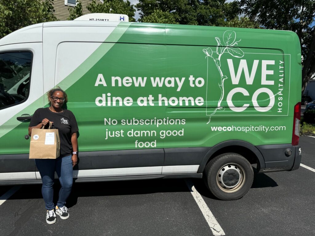 A woman stands in front of a bright green WECO delivery truck. She is holding a brown paper bag, getting ready to make someone happy for dinner.