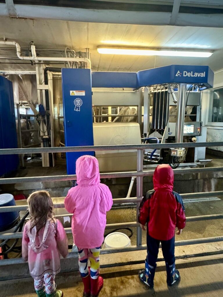 Three kids wearing colorful raincoats check out some high-tech machinery.