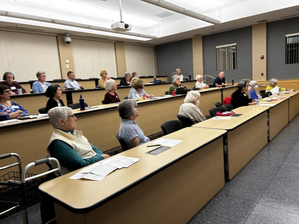 The main meeting room at the Public Safety Building is mostly filled with women (and a few men) who are watching something in the stage area.