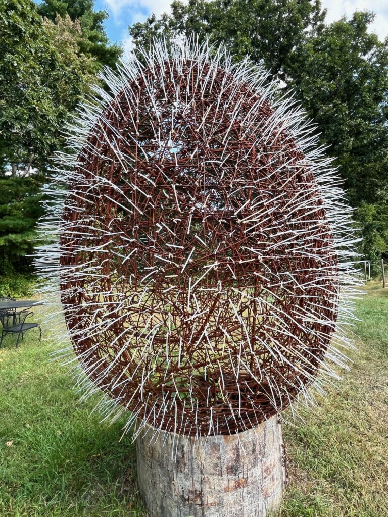 A large egg made of rusted metal and zip ties rests on a pedestal.The Egg is on permanent exhibit near the raspberry patch at Old Frog Pond farm.