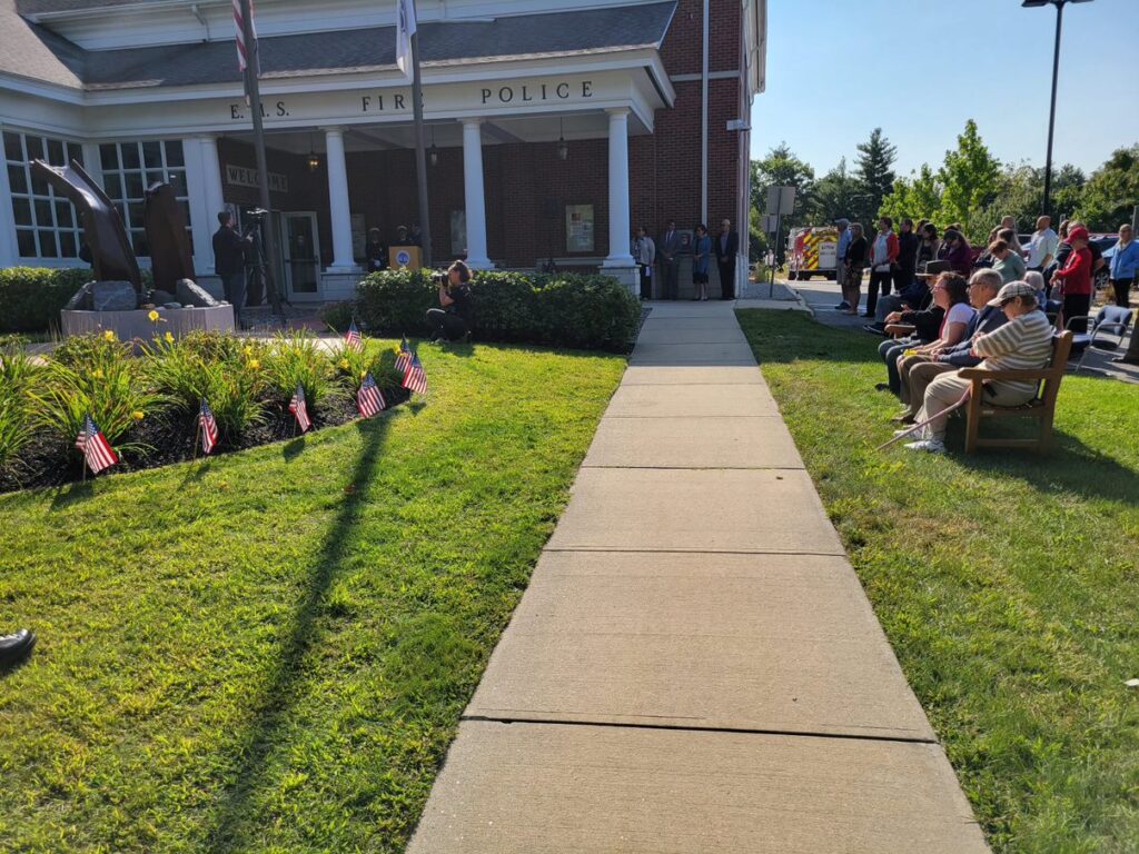 People are seated in chairs on the lawn in front of the Public Safety Building.