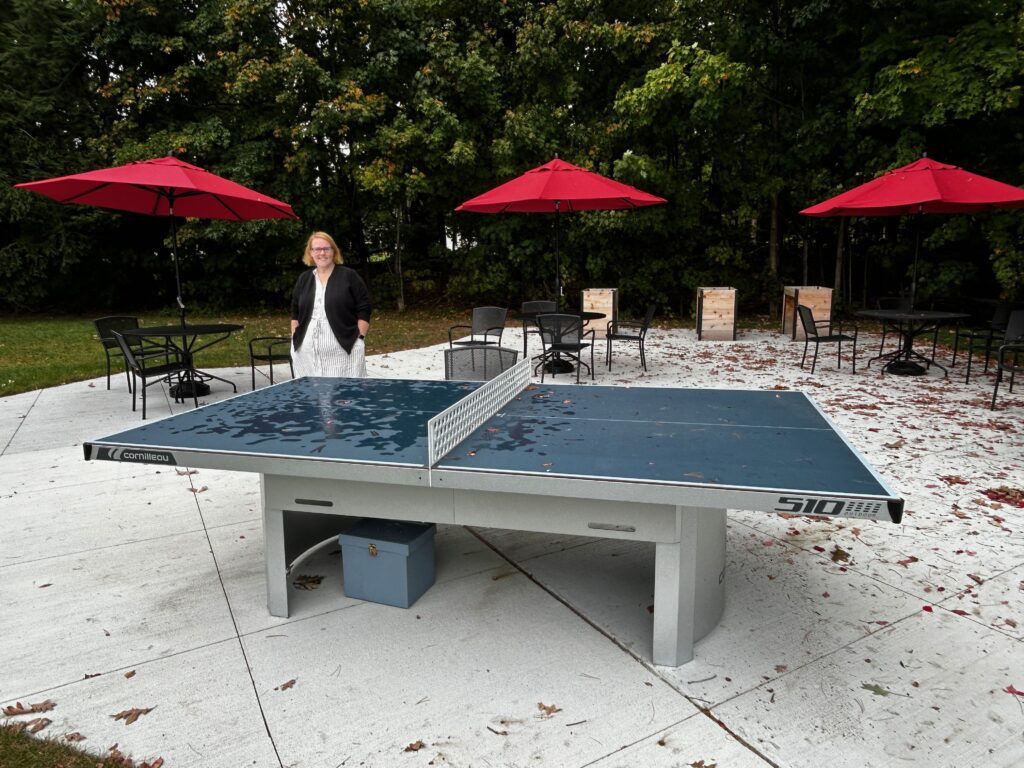 A wonan stands behind a game table on an outdoor patio