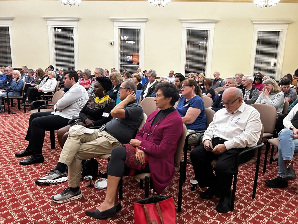 A large room filled with people sitting in chairs and mostly looking at the front of the room.