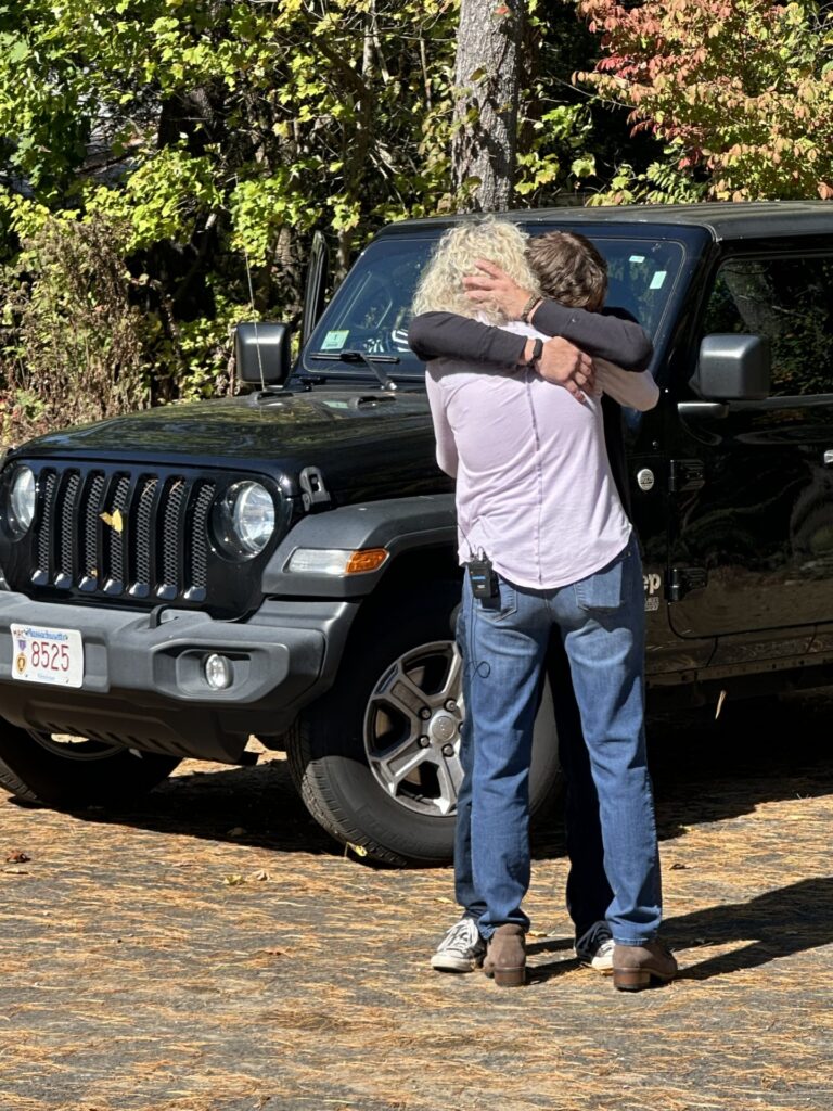 A man tightly hugging a woman on a sunny fall day.