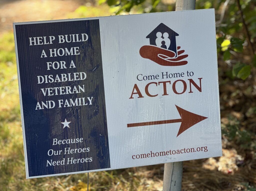 A sign that says: Help build a home for a disabled veteran and family, because our heroes need heroes. Come home to Acton; comehometoacton.org