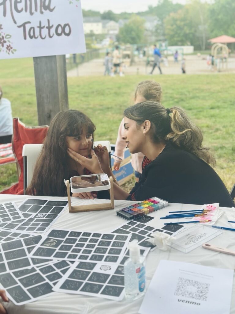 A young girl has her faice painted by a young woman.