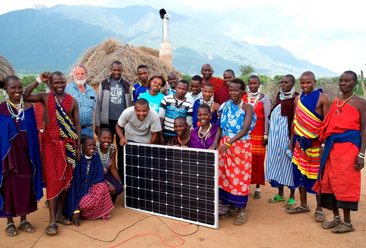 A group of people in Maasai dress (colorful fabric wraps) hold a solar panel.