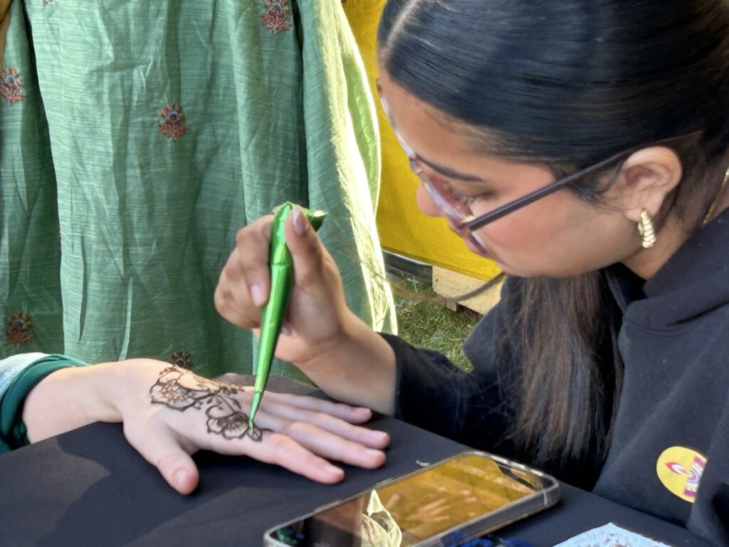 One young womanconcentrates hard as she paints someone's hand with a tube of henna.